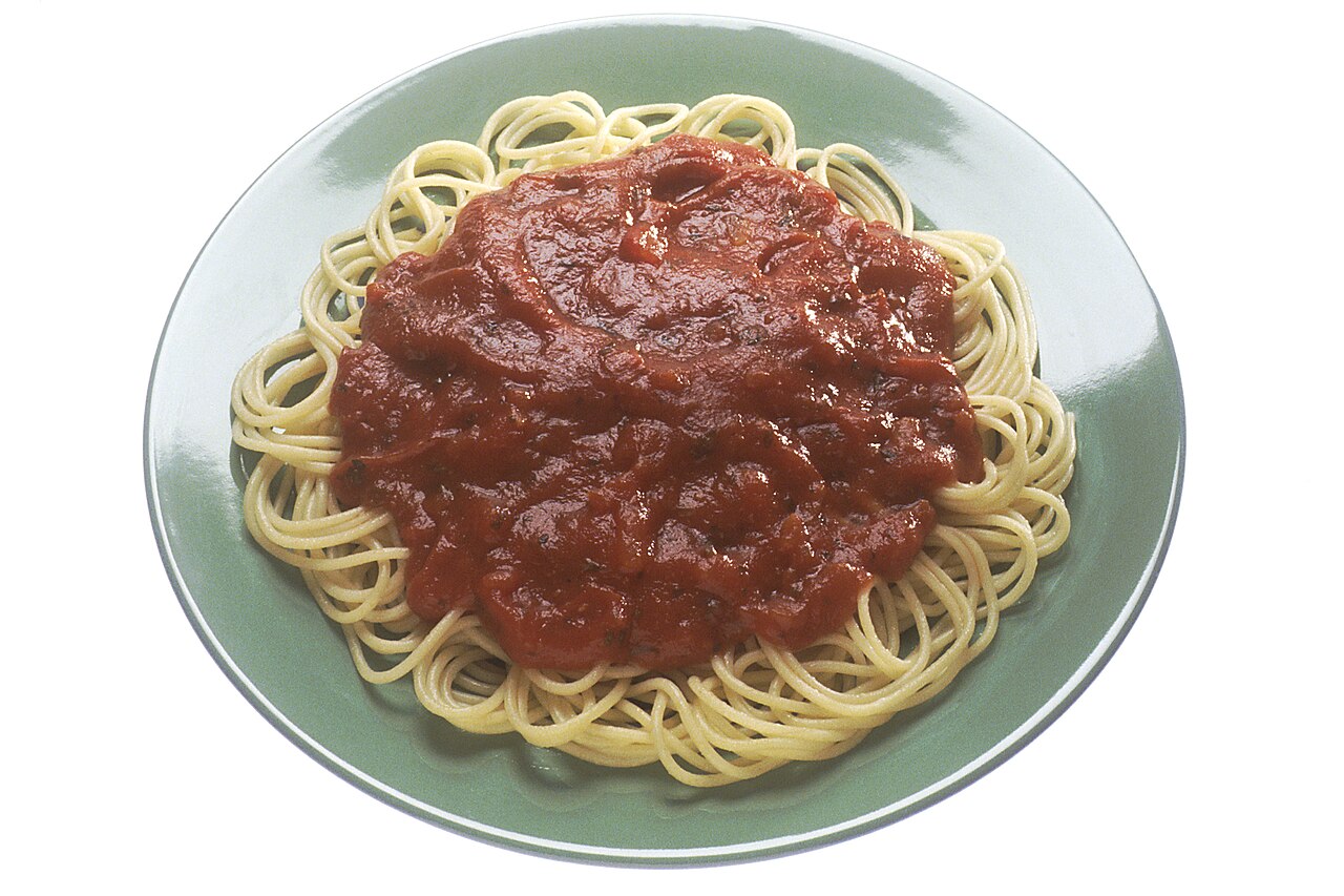 A green plate of cooked spaghetti topped with tomato sauce, seen from above on a white background