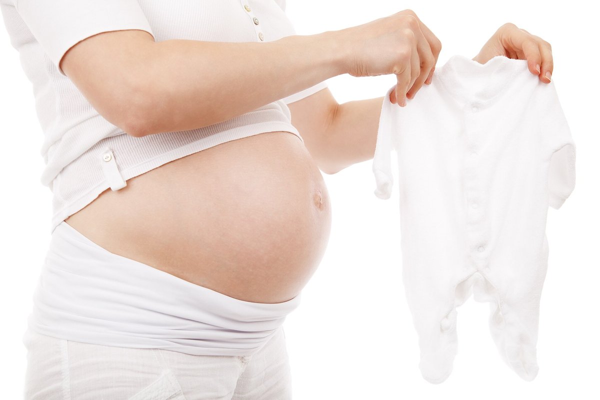 A pregnant woman holds up a white baby sleepsuit