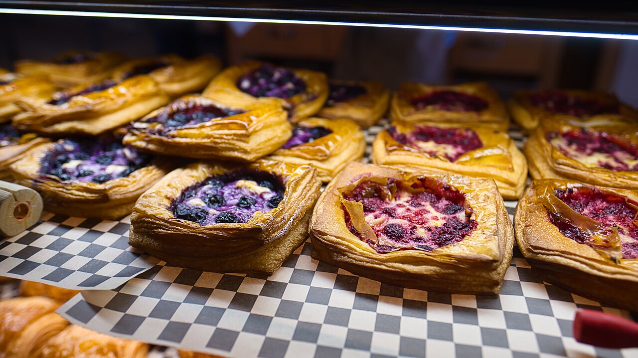 Rows of fruit-filled pastries on checked paper in a bakery display case
