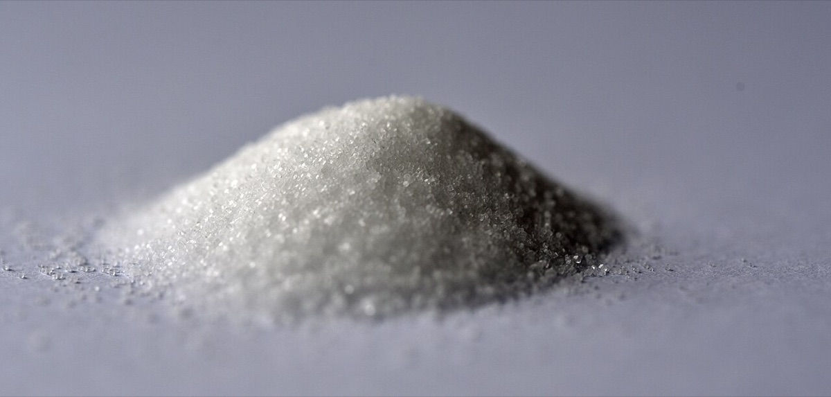 A small heap of fine white table salt on a pale grey surface, close up