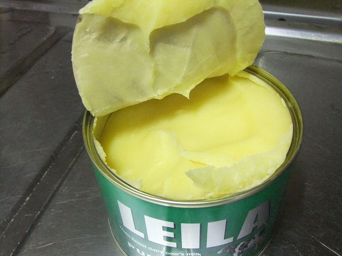 An opened tin of ghee with the solid yellow fat broken at the top