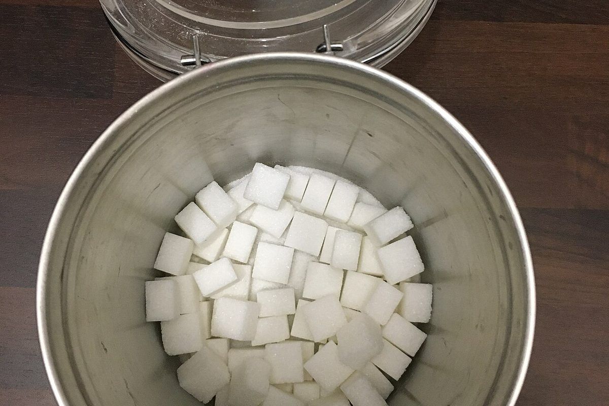 An open metal tin of white sugar cubes, seen from above, on a dark wooden table