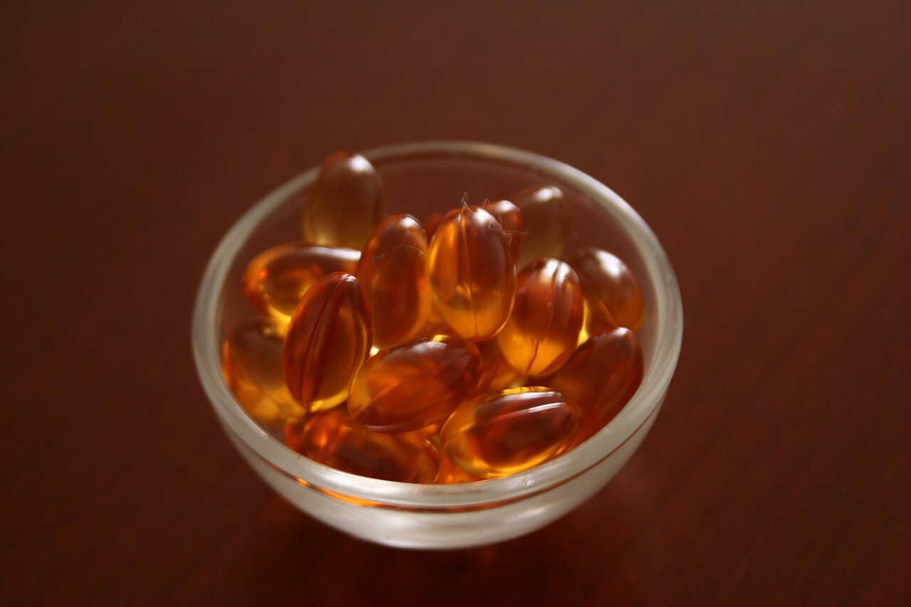 Amber vitamin E gel capsules heaped in a small glass bowl on a dark wooden table
