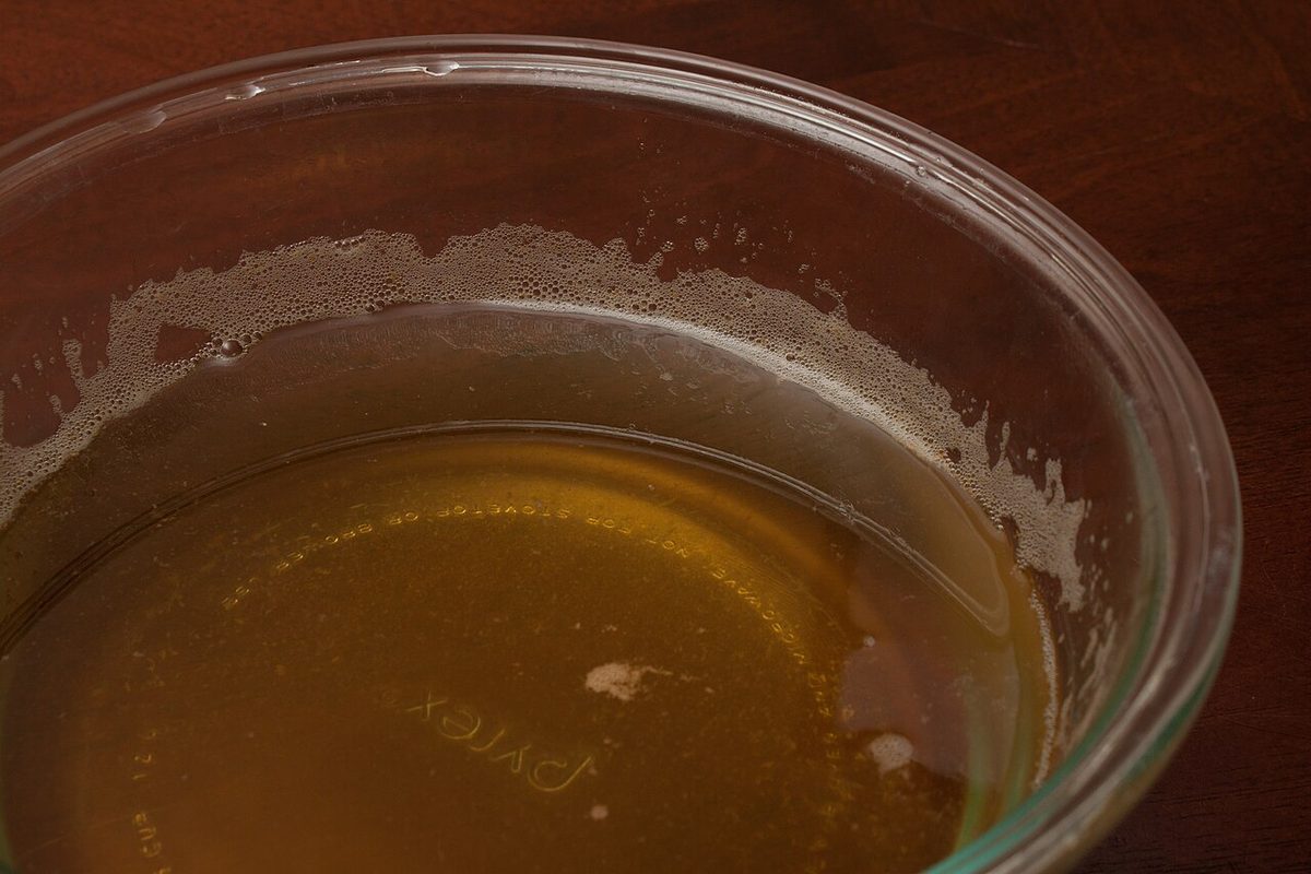 Clear golden vegetable broth in a glass bowl on a dark wooden table